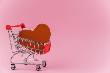 Moda pembe arka planda alışveriş arabasında kırmızı kalp ve metin için fotokopi alanı. Sevgililer günü alışverişi, satış ve aşk için para israfı kavramı 