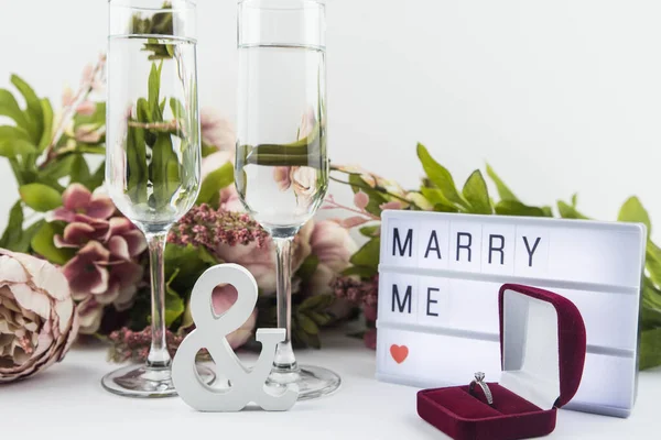 Marriage proposal and love concept for Valentine`s day, box with wedding or engagement ring with brilliant. Glass of champagne, romantic dinner, peony flowers on white background