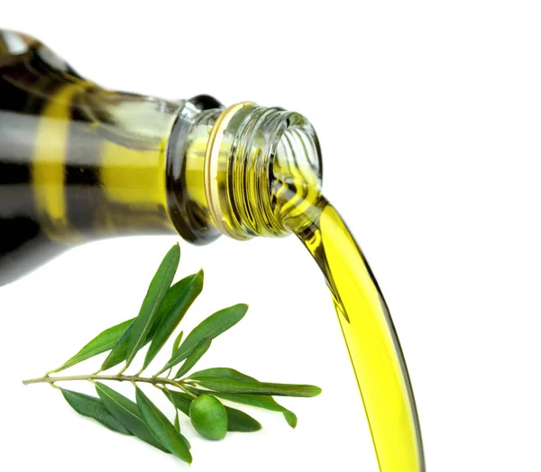 Versare l'olio extravergine di oliva dalla bottiglia di vetro con ramo di ulivo verde . — Foto Stock