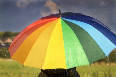 Gökkuşağı renkli şemsiye fırtına bulutları altında olan bir kişi