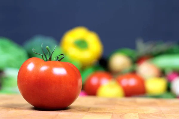 Tomate fraîche sur une planche à découper avec des légumes colorés — Photo