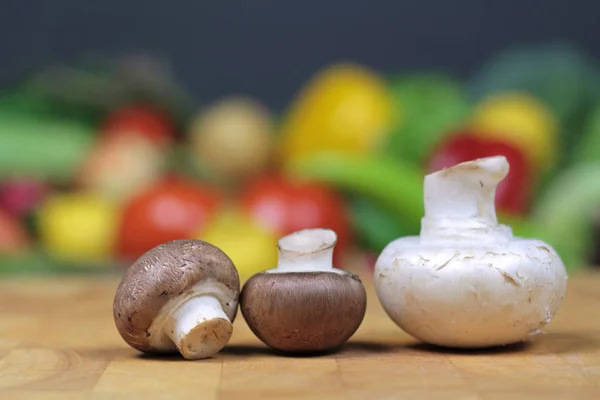 蘑菇上砧板与模糊的蔬菜背景 — 图库照片