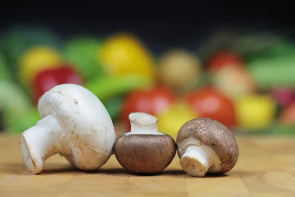 Champiñones sobre tabla de cortar con fondo de verduras borrosas . — Foto de Stock