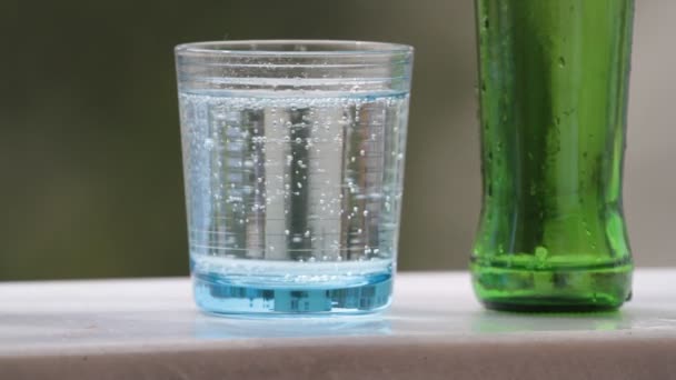 Mineraal water in blauw glas met bubbels en groene glazen flessen — Stockvideo
