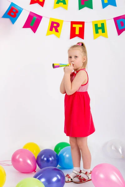 Dziewczynka gospodarstwa gwizdek stoi obok balony napis szczęśliwy urodziny, białe tło — Zdjęcie stockowe