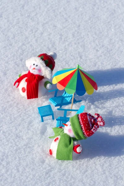 Deux mignons bonhomme de neige bronzant dans la neige. Chaises de plage en papier et parasol. Fond d'hiver — Photo