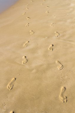Gün batımında kumsal, dalga ve ayak izleri