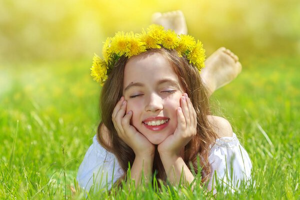 Sweet beautiful girl sitting on a green meadow with dandelions