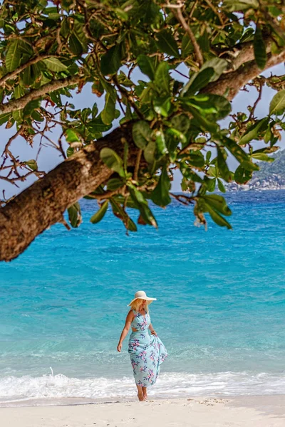 A girl in a blue summer dress with a hat on his head, standing on the white sand. Similan Islands