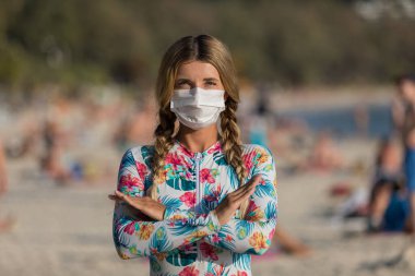 Yüzlerinde koruyucu cerrahi maske takmış bir kadın ve bir çocuk sahilde mayo giymiş duruyor. Çin koronavirüs hastalığı COVID-19 tehlikelidir..