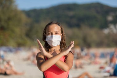 Yüzlerinde koruyucu cerrahi maske takmış bir kadın ve bir çocuk sahilde mayo giymiş duruyor. Çin koronavirüs hastalığı COVID-19 tehlikelidir..