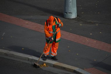 Turuncu üniformalı sokak süpürücü sokağı süpürüyor.
