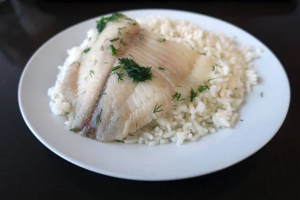 Pilavlı haşlanmış balık ve bir restoranda beyaz bir tabakta dereotu.