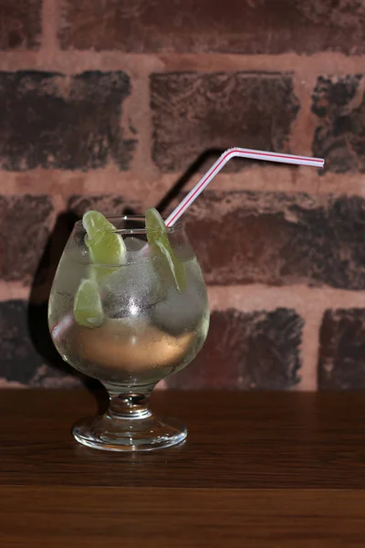 misted glass with cocktail with ice, lime slices and straws against a brick wall