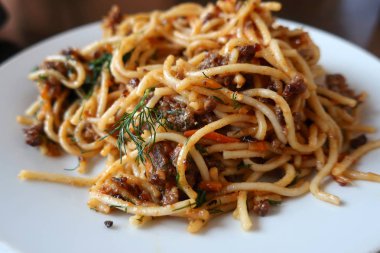 Restorandaki bir masada beyaz bir tabakta kıyma soslu makarna.