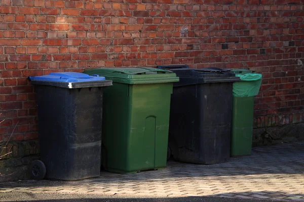 plastic trash cans in the shade of a brick wall