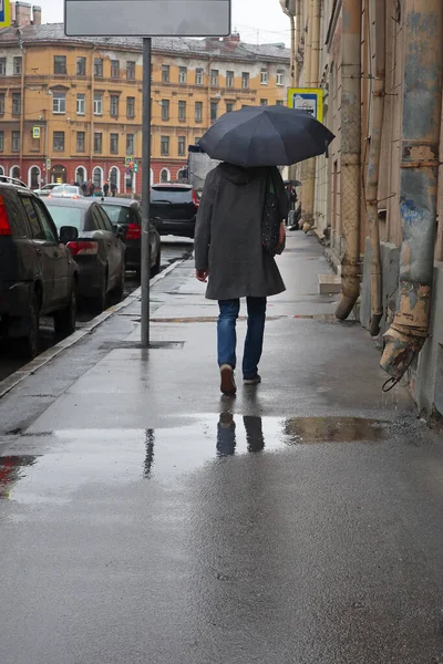 Mężczyzna Torbą Ramieniu Pod Czarnym Parasolem Spaceruje Chodniku Deszczu — Zdjęcie stockowe