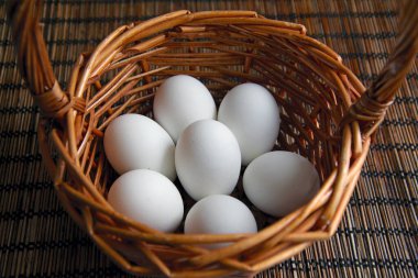 Masadaki hasır sepetinde yedi beyaz tavuk yumurtası.