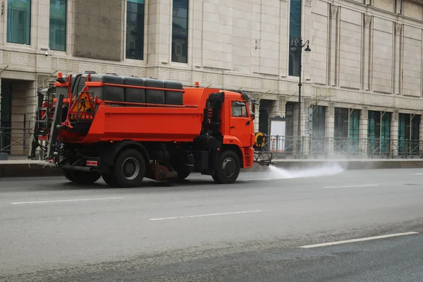 Orangefarbener Lkw Beladen Mit Wasserfässern Die Eine Fahrbahn Bewässern lizenzfreie Stockfotos