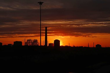 Gün batımında şehir binalarının siluetleri, yüksek voltaj kuleleri, sanayi kuleleri ve ağaçların gölgeleri