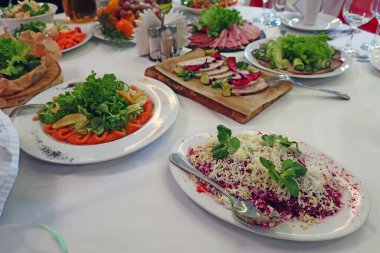 Şirket ziyafeti için çeşitli tabaklar içeren beyaz masa örtüsüyle kaplı bir restoranda bir masa.