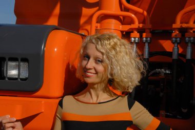 Bir portakal Paletli ekskavatör duran ve neşeli seyir gülümseyen bir genç sarı saçlı kadın portresi.