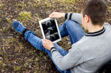 Çocuk çimenlerin üzerinde oturan ve tablet vasıl arıyorum. Modern technolo