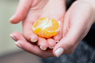 The girl holds a piece of mandarin in her hands. Hands of a girl