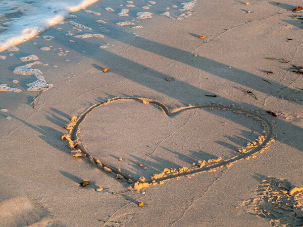 Берег моря, сердце, вытянутое в песок удаляется из волн, закат света