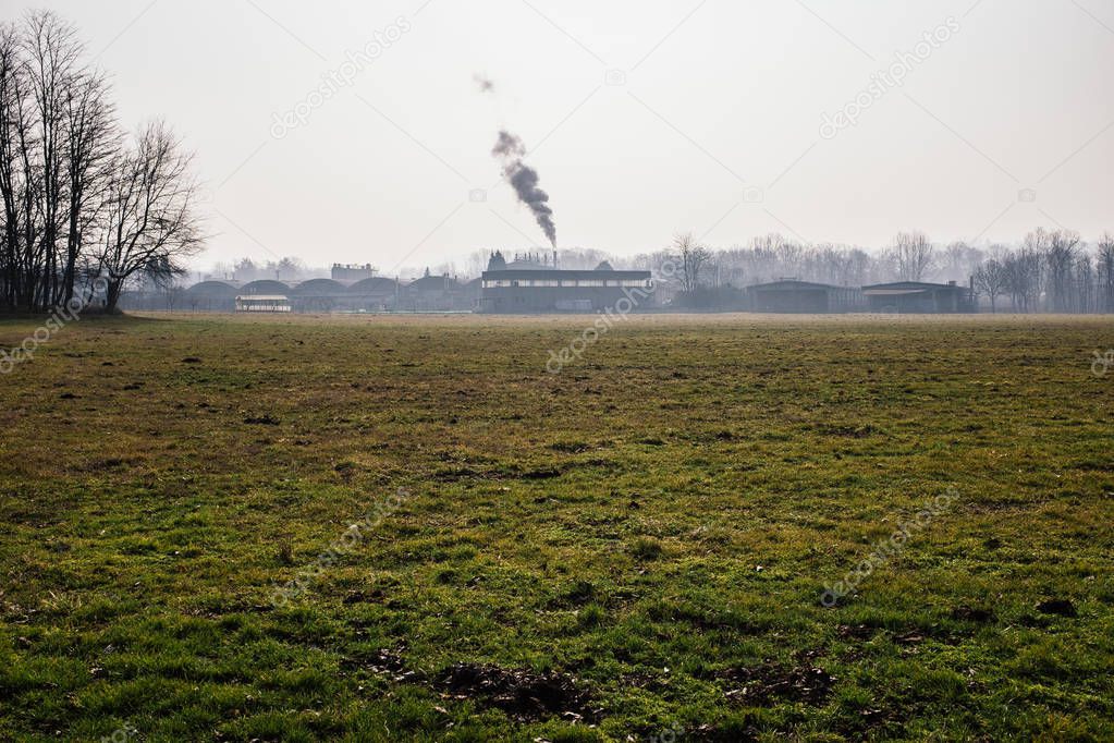 chimney of a factory expels the vapors in the countryside, among green meadows and trees