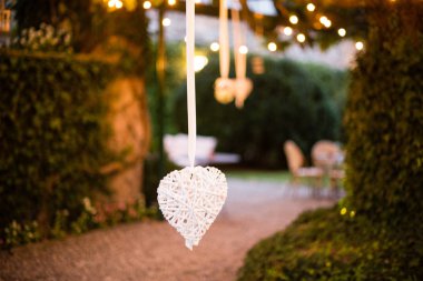 Geniş manolya ağacıyla dolu villa bahçesi. Dallarından sarkan bir sürü fener ve elektrik lambası var. Düğün partisi ya da diğer kutlamalar.