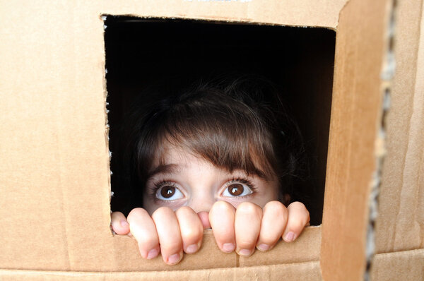 Face of afraid little girl peeking out from a cardboard box