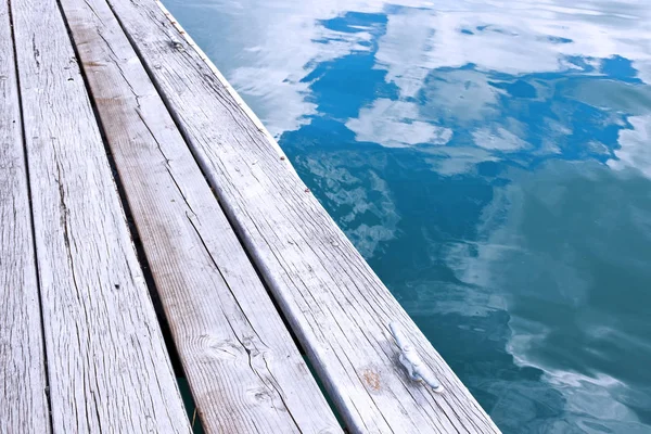 Wooden jetty pier and reflection of sky in blue water — Stock Photo, Image