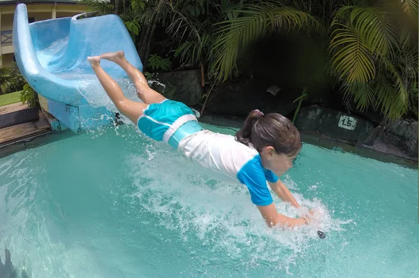 Menina jovem salpicando na piscina depois de descer a corrediça de água — Fotografia de Stock