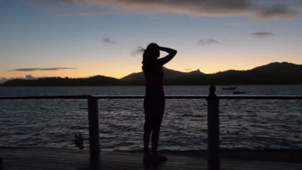 Силует молодої жінки, яка спостерігає за заходом сонця — стокове відео
