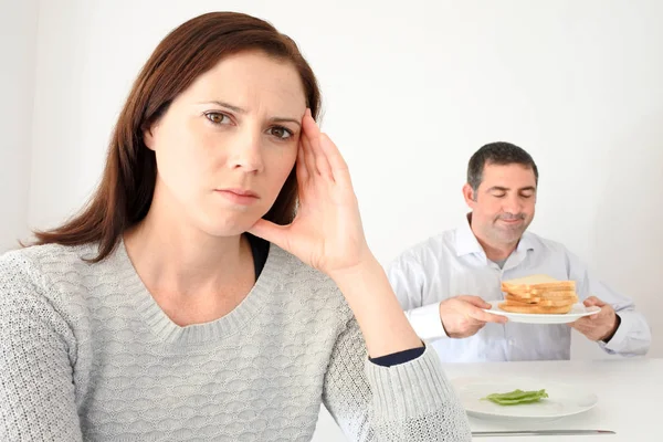 Молода жінка засмучена, коли її партнер їсть і насолоджується вуглеводами — стокове фото