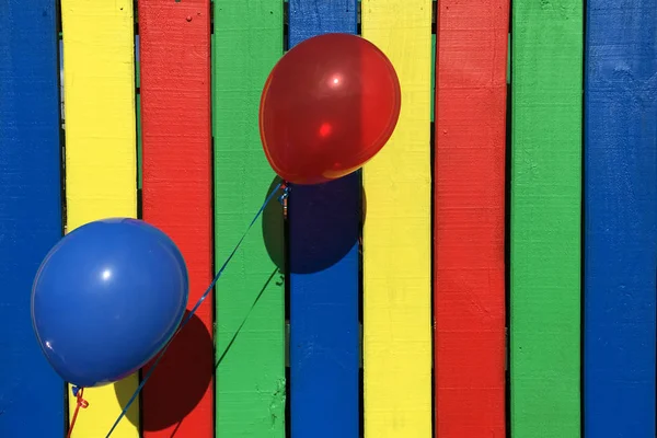 Balão azul e vermelho em uma cerca colorida — Fotografia de Stock