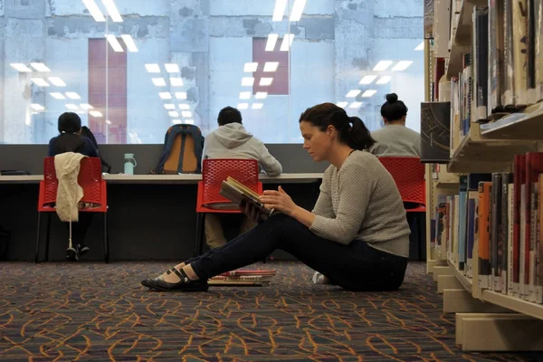 Estudante do sexo feminino lendo um livro em uma biblioteca — Fotografia de Stock