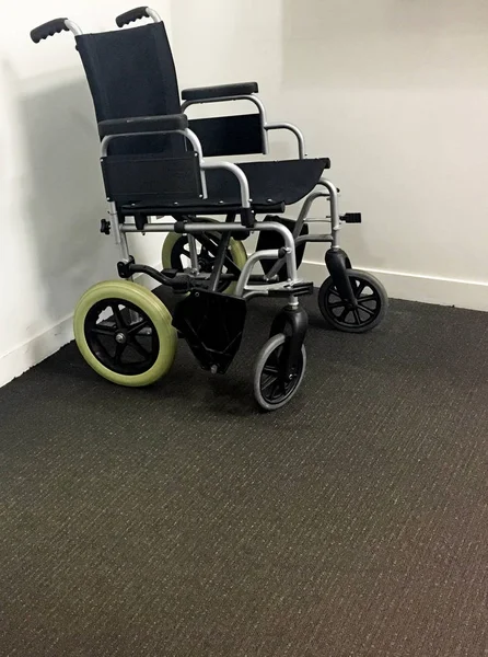 Чёрное инвалидное кресло в углу больничной палаты — стоковое фото