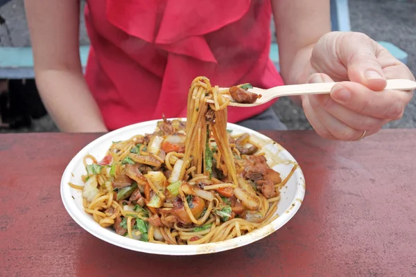 Woman eats Asian noodels dish served in a plate in Rarotonga nig — Stock Photo, Image