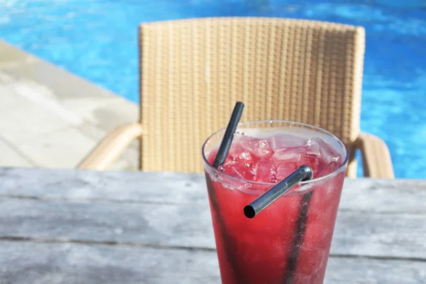 Red cocktail drink with ice served on a poolside table in a trop