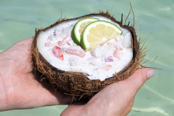 Frau hält Ceviche-Gericht in Kokosnuss über Lagunenwasser — Stockfoto