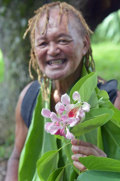 Happy Olde aged Pacific Islander man gives an exotic flower on e — Stock Photo, Image