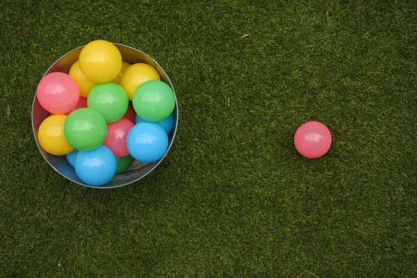 Bola rosa fora de um balde cheio de bolas coloridas na grama verde — Fotografia de Stock