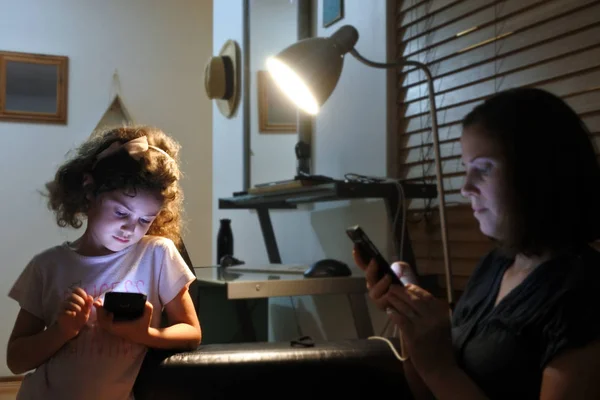 Young girl and mother reading messages on cell phone in home at n — стоковое фото