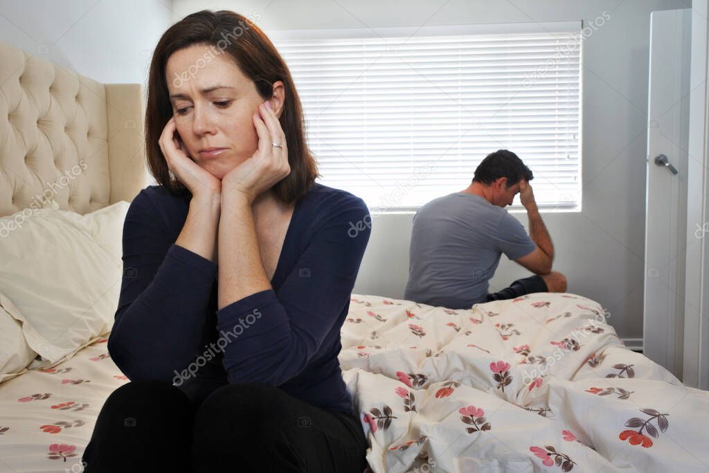Sad couple in home bedroom. woman sitting on bed while in the background a man