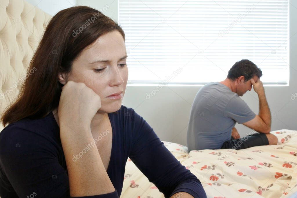 Sad couple in home bedroom sitting on bed.