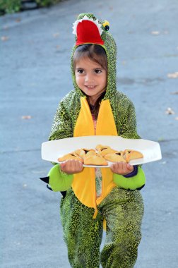 Yahudi kız (5 yaşında) timsah kostümü giyerek Purim Yahudi Tatili için Oznei haman 'lı Mishloach Manot (Purim sepeti) taşır..