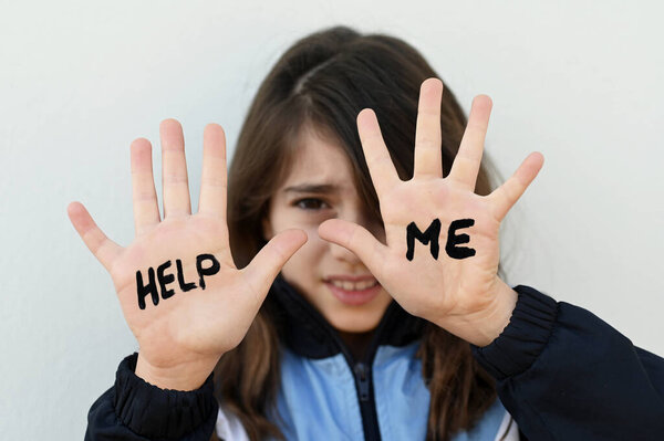 Young girl (age 10) being bullied in school protecting her face with her hands with the words Help Me.
