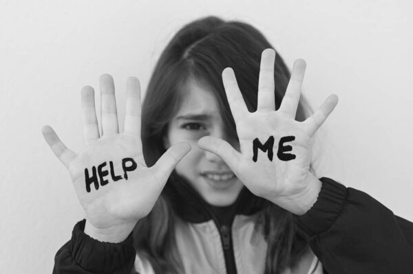 Young girl (age 10) being bullied in school protecting her face with her hands with the words Help Me.